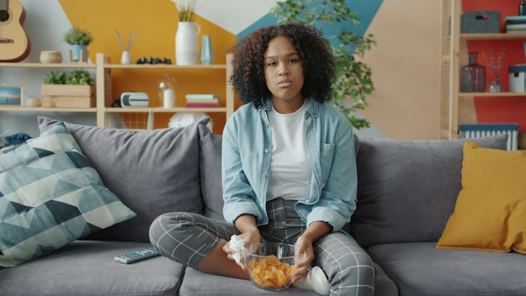 Young woman on a sofa with a bowl of snacks and a TV remote, ready to watch