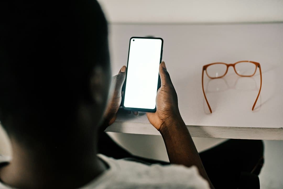 Person holding an Android smartphone with a blank screen at a desk