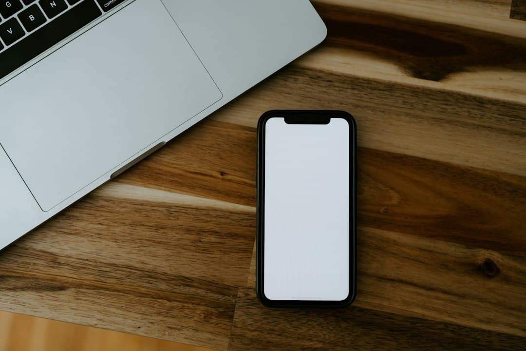 Smartphone with a blank screen lying on a wooden desk next to a laptop